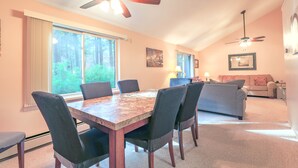 A dining area with a wooden table and chairs, a ceiling fan, and large windows with curtains.