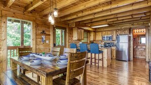 Una cabaña de madera con comedor, cocina y ventanas amplias.