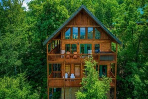 Une cabane en rondins à deux étages, dotée de plusieurs balcons et entourée d’une forêt dense.