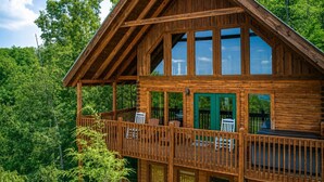 Una cabaña de madera con balcón, ventanas amplias y vistas al bosque.
