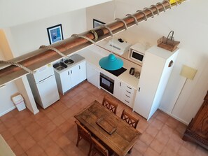 Eine kompakte Küche mit weißen Schränken, einem Holztisch und einem regalartigen Hängegestell.