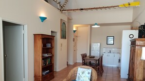 A spacious living area with a wicker chair, a wooden bookshelf, and a dining table with chairs.