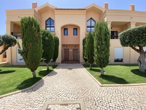 A two-story building with a symmetrical facade, a central entrance with a door, and a paved driveway leading to the entrance.