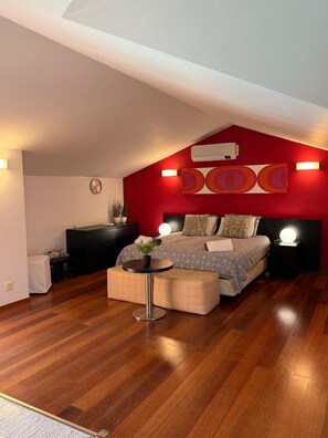 A bedroom with a bed, bedside tables, a round table, and a red accent wall.