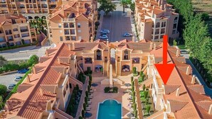 A hotel with multiple balconies, a central swimming pool, and a landscaped garden area.
