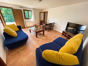 Uma sala de estar com dois sofás azuis, uma mesa de centro, uma televisão e um espaço de jantar com cadeiras e mesa.
