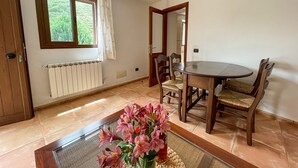 Ein Essbereich mit einem runden Tisch, vier Stühlen, einem Heizkörper, einem Fenster mit Vorhängen und einer Tür.