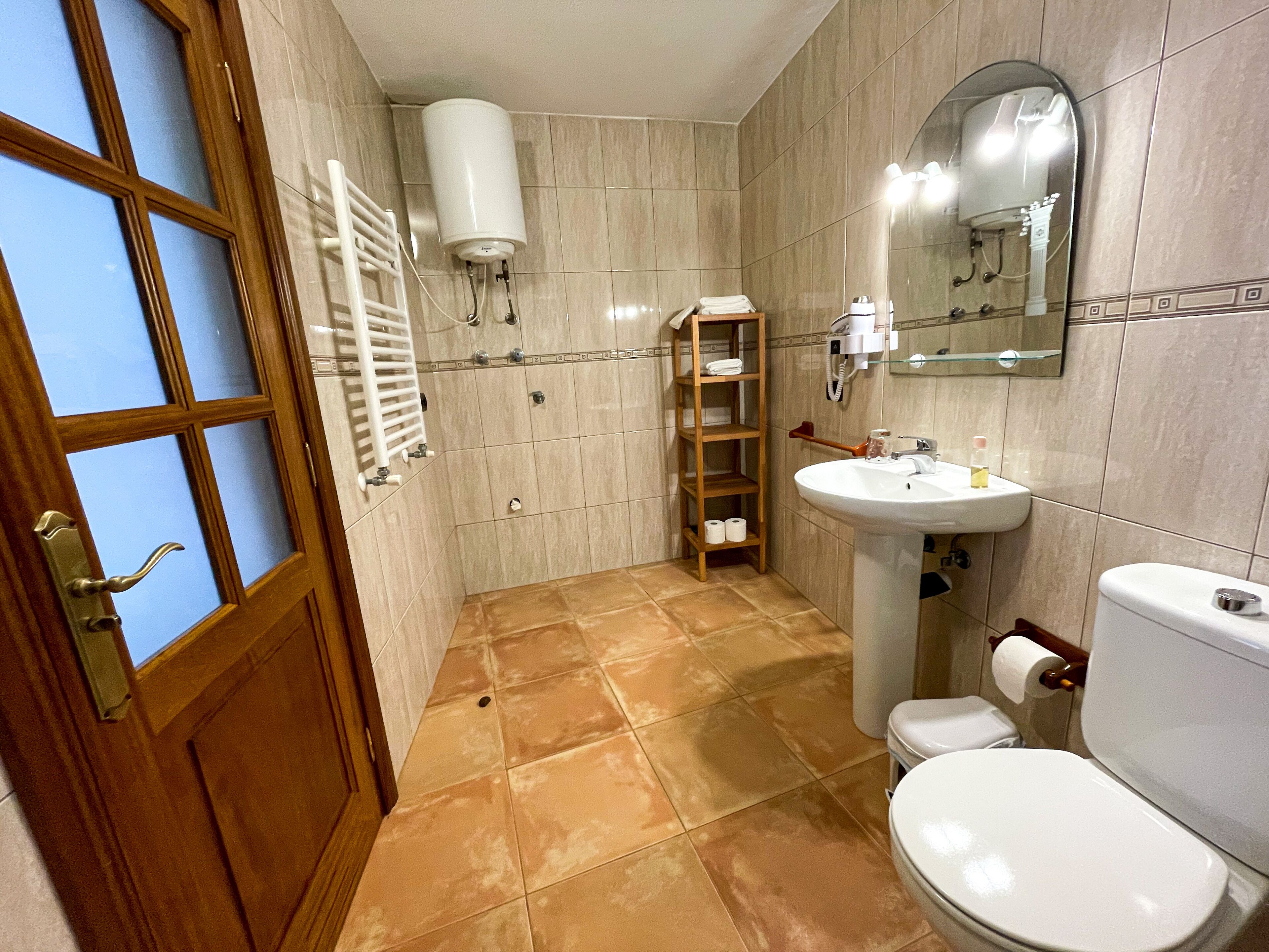 Un baño con inodoro, lavamanos, espejo, toallero y zona de ducha.