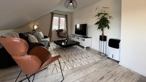 Moderni olohuone, jossa on sohva, ruskea nojatuoli, televisio, sohvapöytä ja ruukkukasvi.