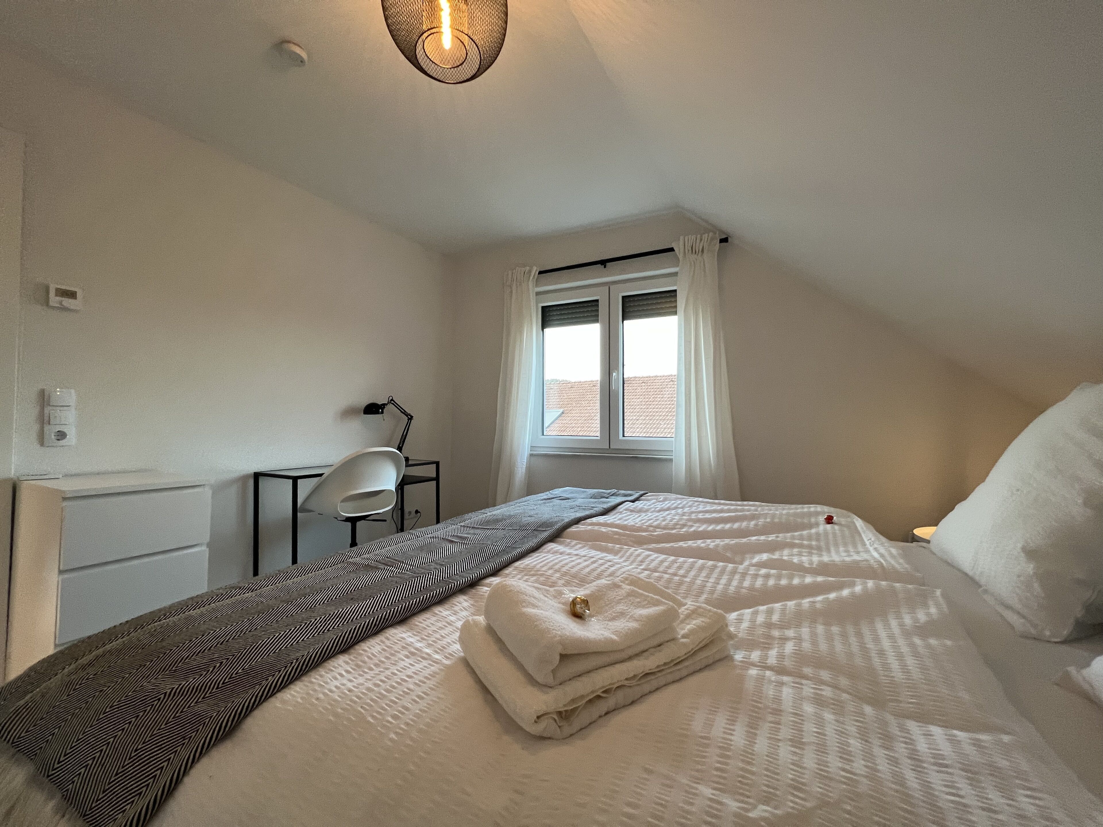 Een slaapkamer met een bed, een bureau, een stoel en een raam met gordijnen.