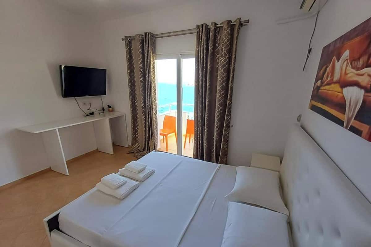 A hotel room with a bed, a desk, a television, and a painting.