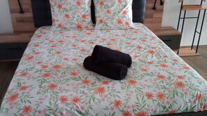 A bed with a floral bedspread and two pillows, a wooden headboard, and a small bedside table with a lamp. - Audrey and Etienne's (Présailles)