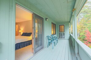A room with a bed, a sliding glass door, and a balcony with chairs.