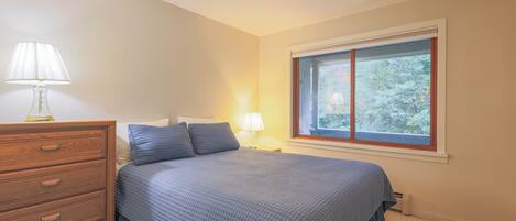 Un dormitorio con cama, cómoda, ventana con vistas y lámpara.