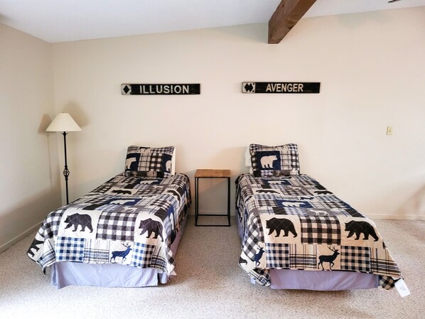 A bedroom with two beds, each with a bear-themed bedspread, a lamp, and two signs on the wall reading "ILLUSION" and "AVENGER".