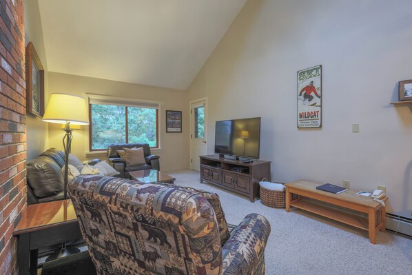 A living room with a sofa, a television, a brick wall, and a poster on the wall.