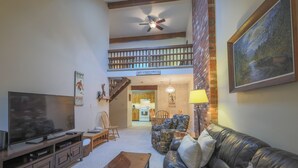 A spacious living room with a flat-screen TV, leather sofa, and a dining area with chairs.