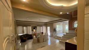A spacious living area with a large window, a sofa, a dining table, and a staircase leading to an upper level. - Panorama Hills Villa (Pylaia-Chortiatis)