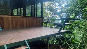 Una terraza de madera con un banco, rodeada de abundante follaje.