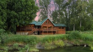 Une cabane en bois avec un toit vert, une véranda et un petit ruisseau qui la borde.