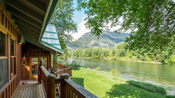 Une cabane en bois dotée d’une terrasse offrant une vue sur une rivière et des montagnes.