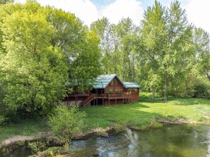 A cabin with a deck, surrounded by trees and a stream.