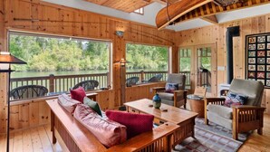 Une cabane en bois avec une grande fenêtre, un canapé, une table et des chaises.