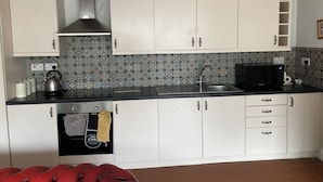 A compact kitchen with white cabinets, a stainless steel range hood, a black microwave, and a patterned backsplash.