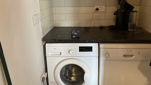 A compact kitchen with a washing machine, a coffee maker, and a water dispenser on the countertop.