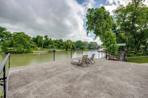 Eine Betonplattform mit Stühlen bietet Blick auf ein Gewässer, umgeben von Bäumen und einem kleinen Pavillon.