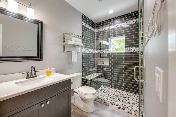 Une salle de bain avec une douche à parois de verre, des toilettes blanches, un meuble-lavabo avec un miroir et un évier.