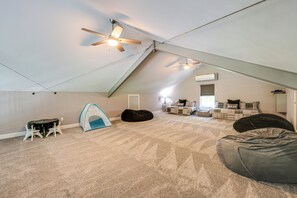 Ein Dachzimmer mit schrägem Dach, Deckenventilator, Sitzsack, Spielzelt und einer Couch.