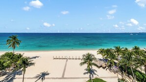 Uma praia com águas turquesa cristalinas, palmeiras e uma fileira de espreguiçadeiras viradas para o mar.