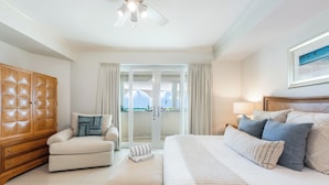 Quarto com cama, sofá, guarda-roupa de madeira e vista através de uma porta de vidro.