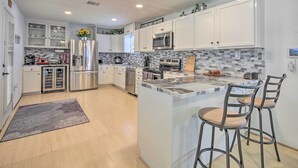 Cocina moderna con armarios blancos, electrodomésticos de acero inoxidable, una isla de mármol y dos taburetes de bar.