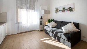 A modern living room with a black sofa, white cushions, a side table with a lamp, and a wall-mounted plant shelf. - Convenient for motorway (Però exit) and for those using public transport ( Però) (Pero)