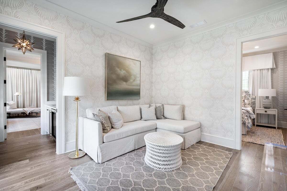 A modern living room with a white sectional sofa, a round white ottoman, and a patterned rug.
