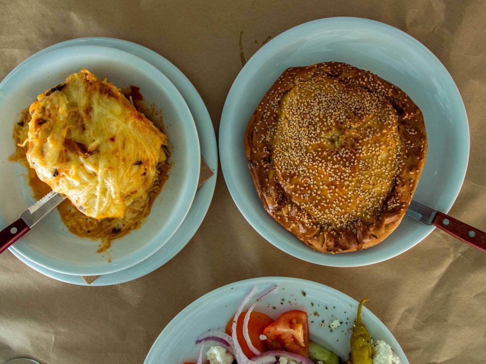 Two plates of food, one with a baked dish and the other with a sesame seed-topped item, on a table.