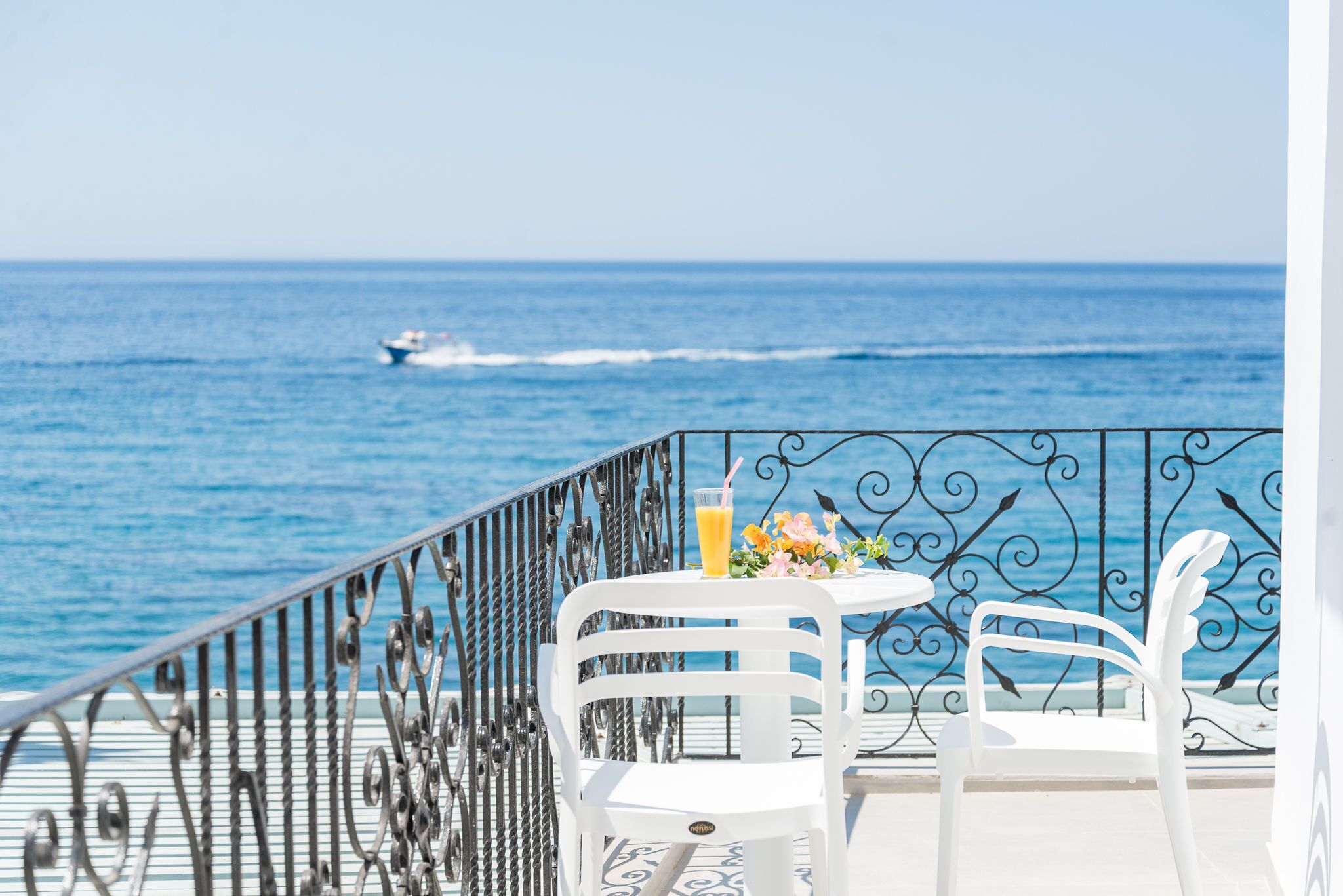 Ein Balkon mit Tisch und Stühlen, mit Blick auf den Ozean, in der Ferne ein Boot.