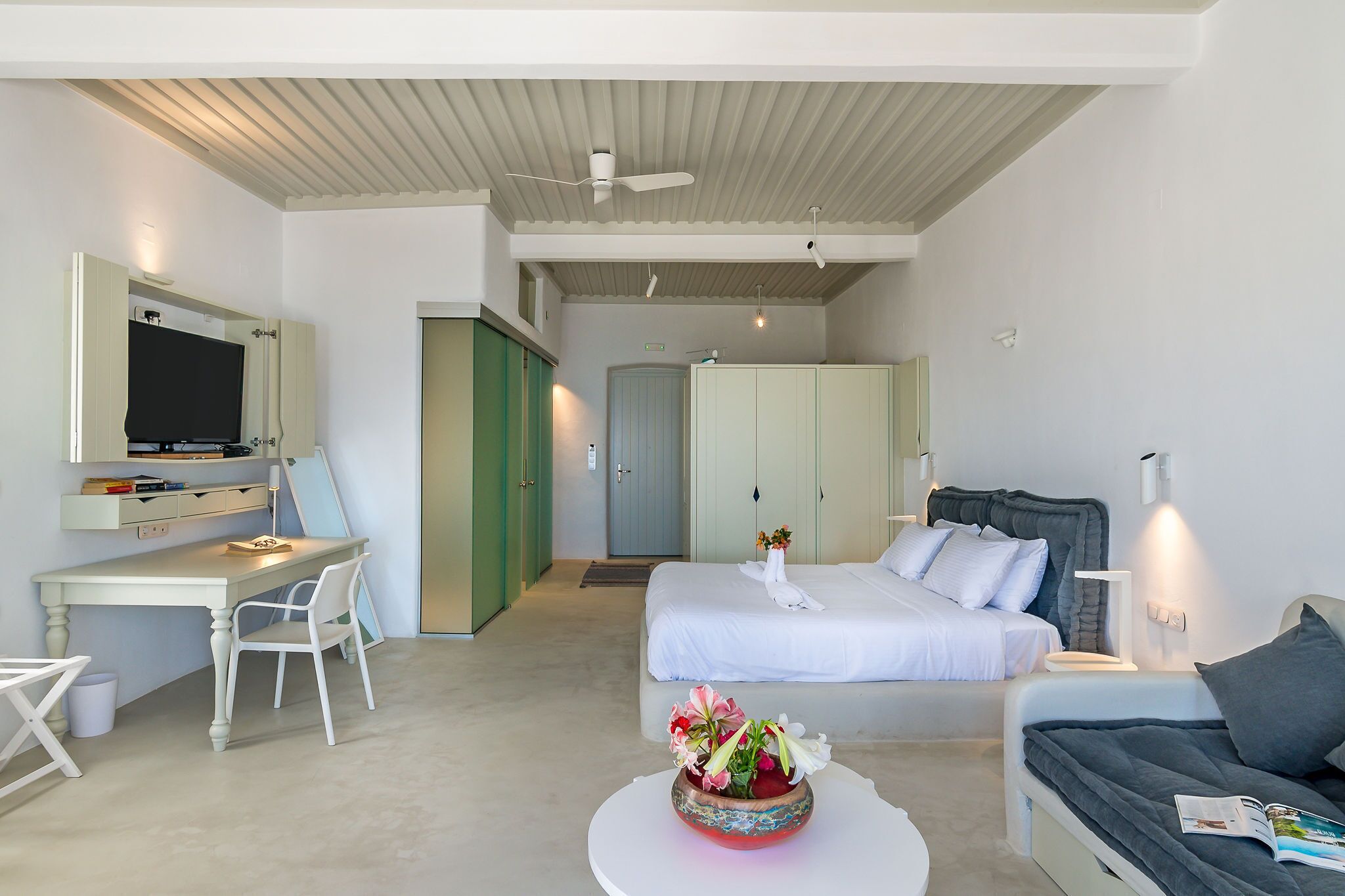 A modern hotel room with a bed, a desk, a chair, and a small table with flowers.