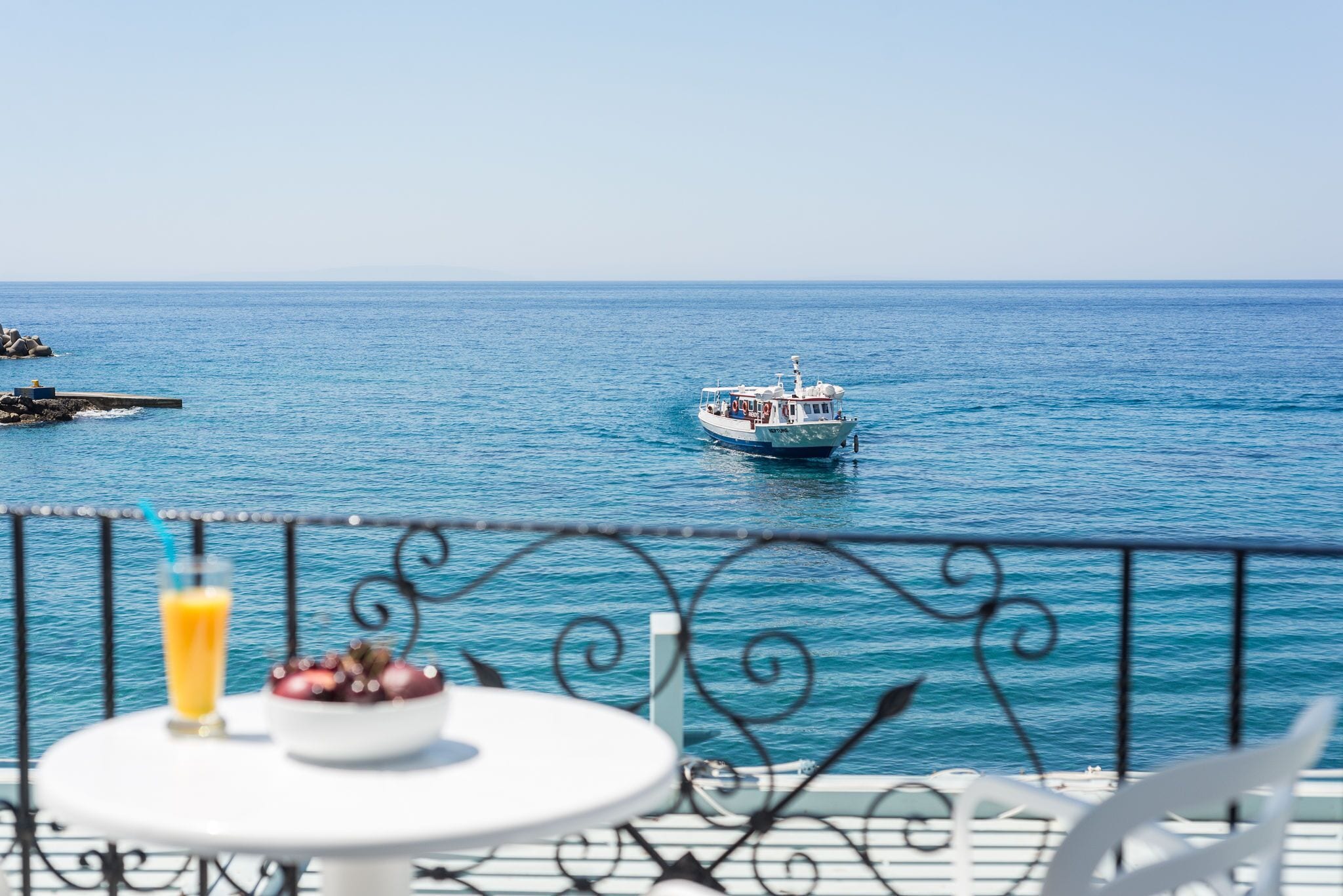 A balcony with a table, a glass of orange juice, and a bowl of fruit.