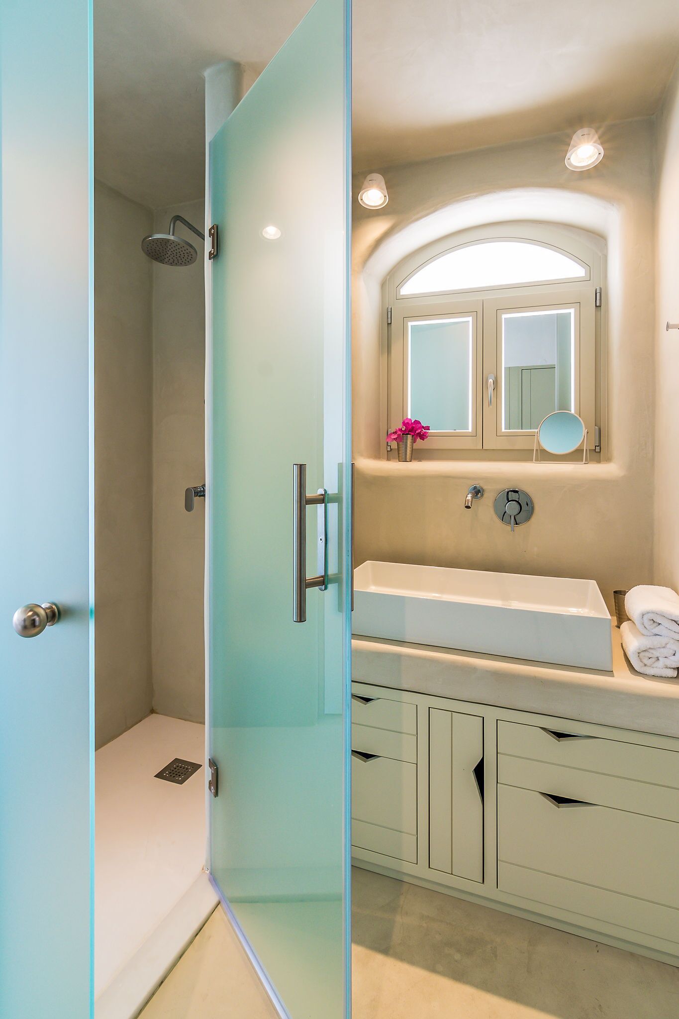 A modern bathroom with a glass shower enclosure, a white sink, and a vanity with drawers.