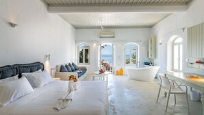 A modern hotel room with a large bed, a sofa, a desk, and a bathtub. There are large windows and a view of the ocean. - Samaria by the Sea (Sfakia)