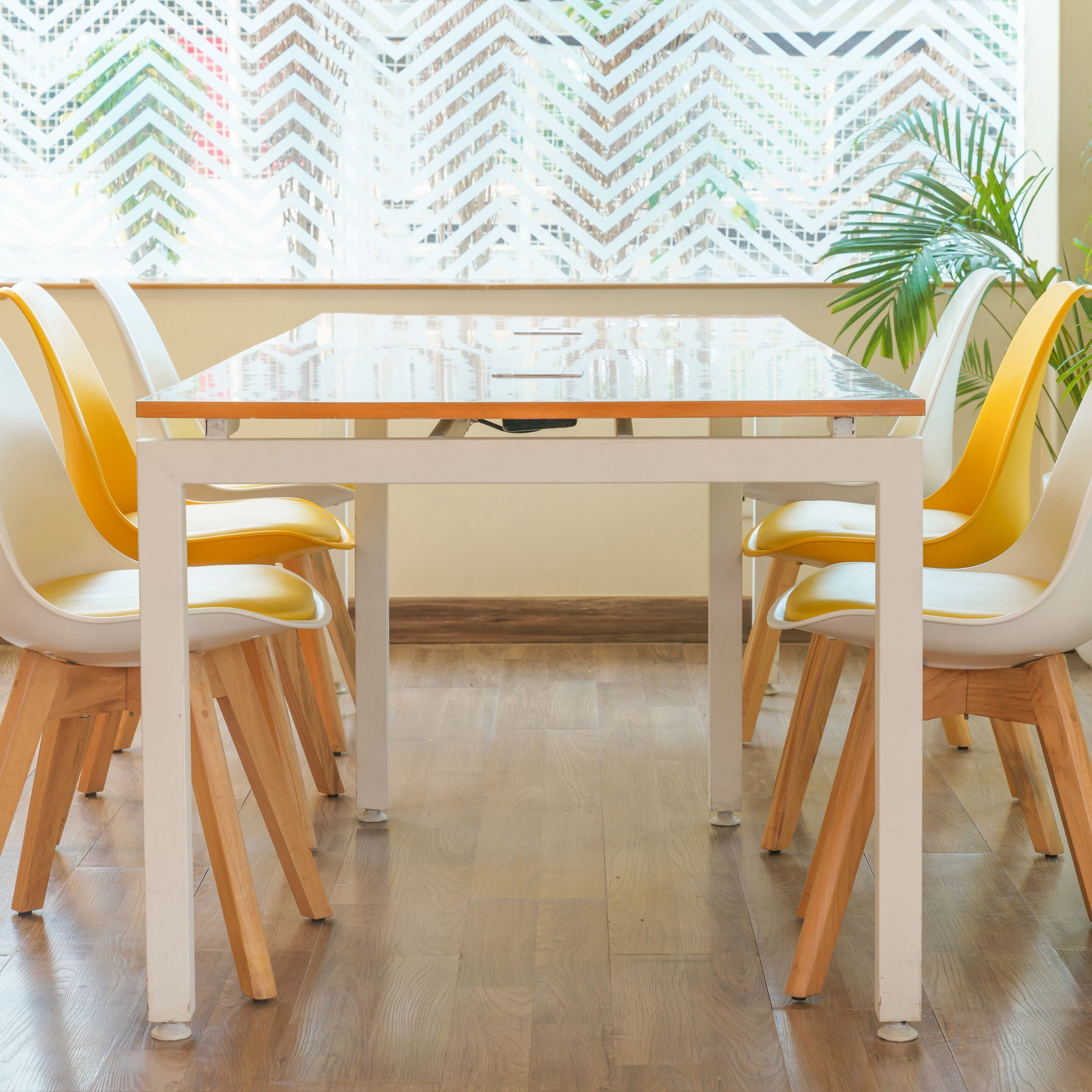 Un coin repas avec une table à plateau en verre, des chaises en bois et une fenêtre offrant une vue sur un paysage aux motifs variés.