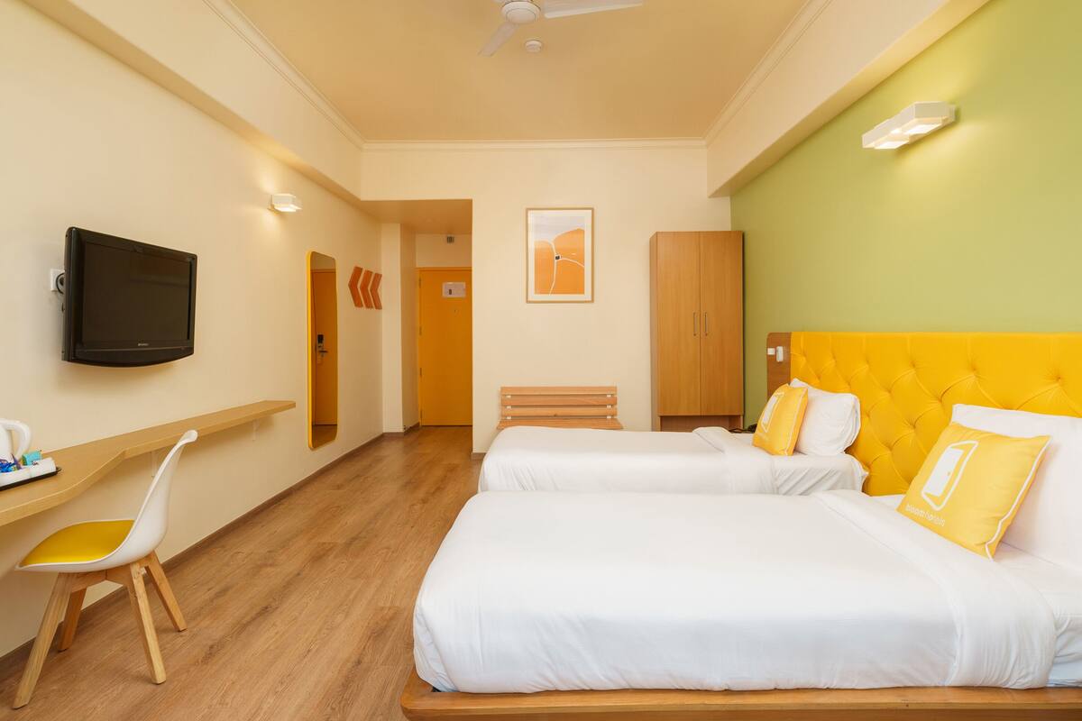 Habitación de hotel con dos camas, un escritorio, una silla, un televisor y un ventilador de techo.