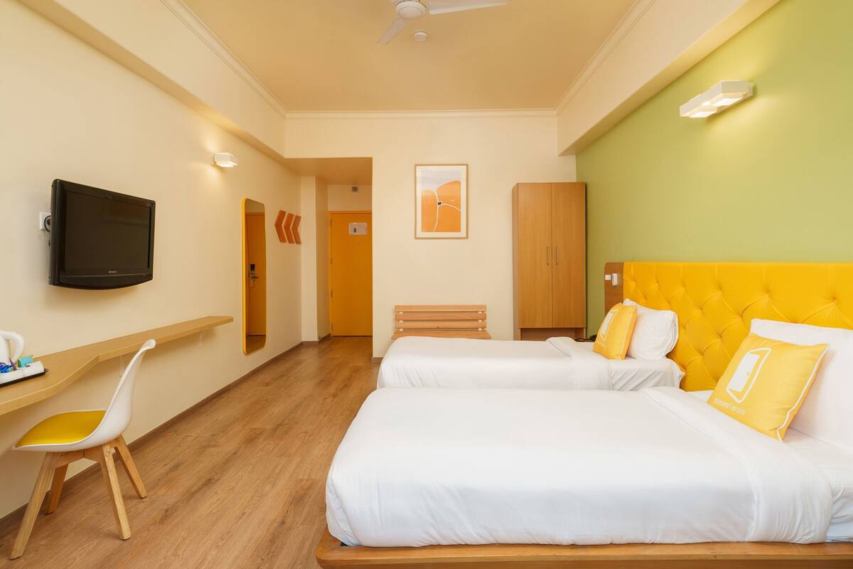Una habitación de hotel con una cama, un escritorio, una silla, un televisor y un ventilador de techo.