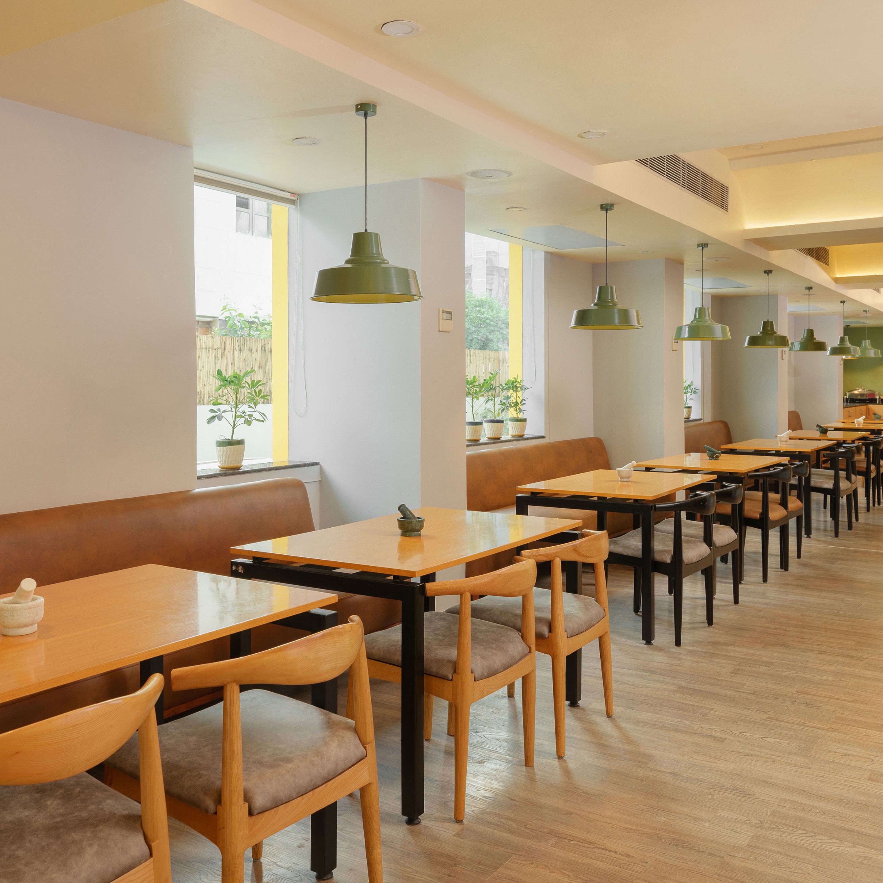 A restaurant with wooden tables and chairs, green pendant lights, and potted plants.