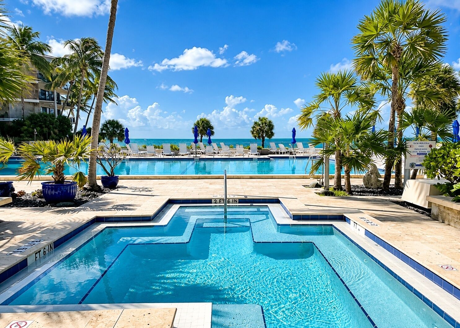 A swimming pool with a view of the ocean, surrounded by palm trees and lounge chairs.