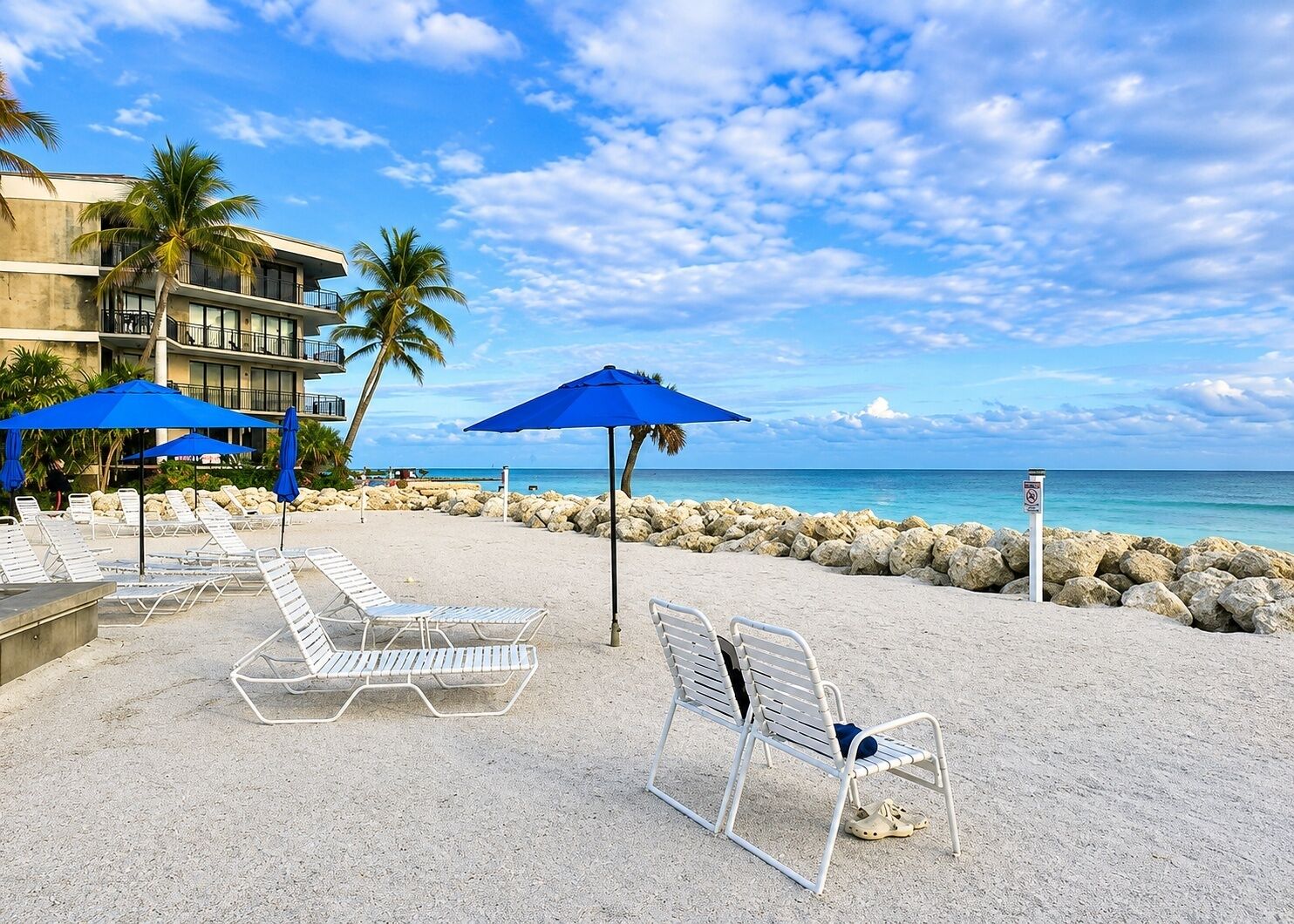 Un hôtel situé en bord de mer, doté de chaises longues, de parasols et offrant une vue sur l’océan.