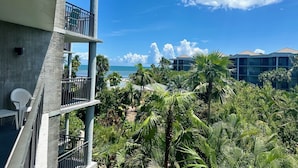Een meerlaags hotel met balkons met uitzicht op een strand en zwembad, omgeven door weelderige begroeiing.